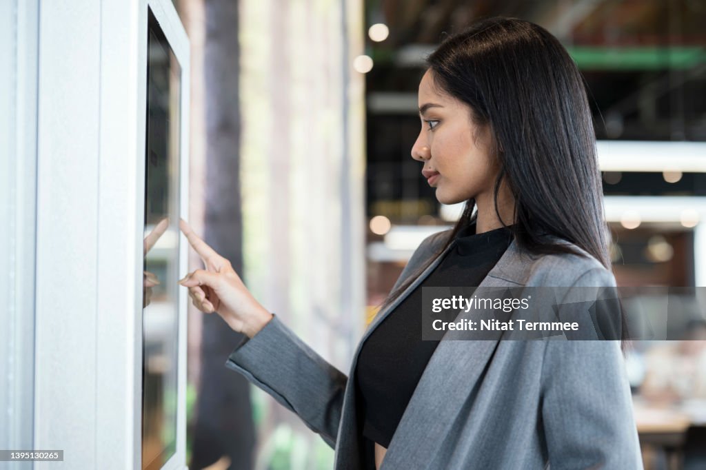 Innovative Framework for Self-service Kiosks Solution. Businesswomen using touch screen display to confirm order or payment of product, service at a kiosk machine.