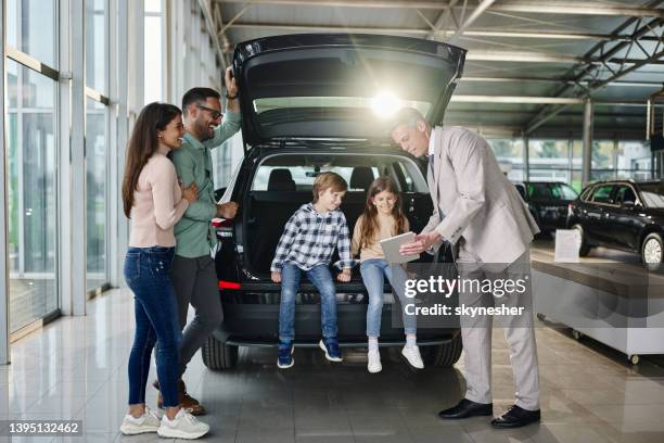young happy family and male salesperson using digital tablet in a car showroom. - buying a car 個照片及圖片檔
