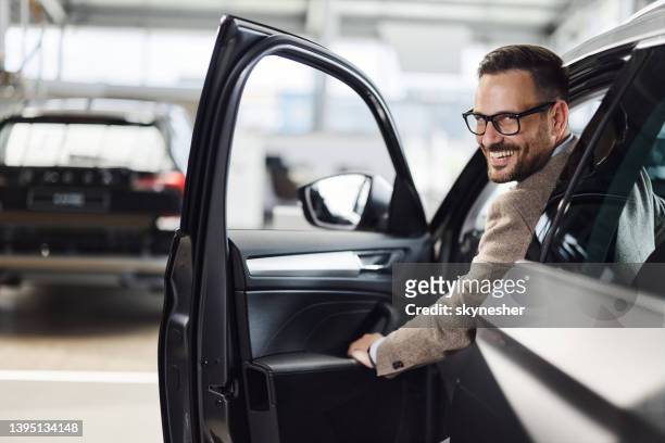 junger glücklicher mann in einem auto im ausstellungsraum. - auto mieten stock-fotos und bilder
