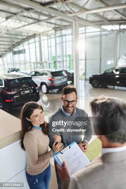 happy couple talking about buying plan with car salesperson in a showroom. - showroom stock pictures, royalty-free photos & images