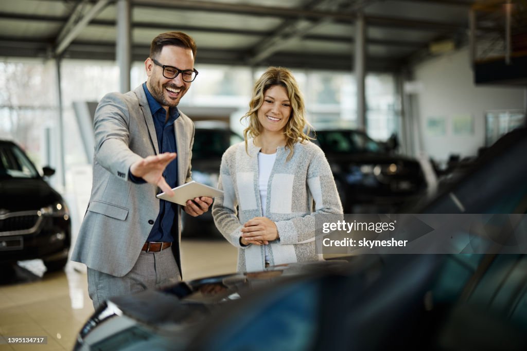 Venditore felice che vende l'auto alla sua cliente in uno showroom.