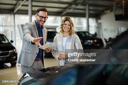 Happy salesman selling the car to his female customer in a showroom. Happy salesman selling the car to his female customer in a showroom.