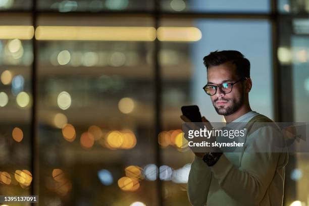junger ernsthafter mann, der im dunkeln eine sms auf dem smartphone liest. - smartphone office stock-fotos und bilder
