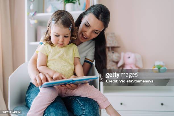 mother and her little daughter reading a book. - mystical baby girls stock pictures, royalty-free photos & images