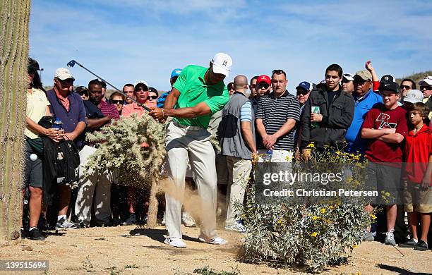 Tiger Woods hits left-handed out of a waste area on the second hole as a gallery of fans look on during the first round of the World Golf...