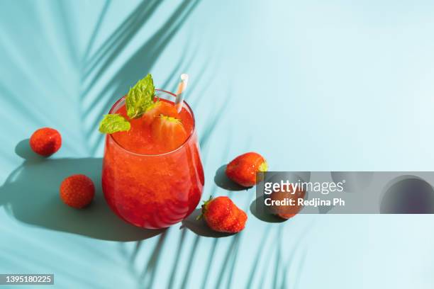summer refreshing sparkling drink with melted ice, fresh strawberry and drinking straw and mint in transparent glasses on blue background. - sparkling water photos et images de collection