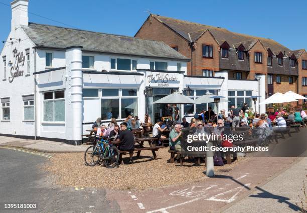 People sitting in sunshine outside the Jolly Sailors pub, Pakefield, Lowestoft, Suffolk, England, UK.