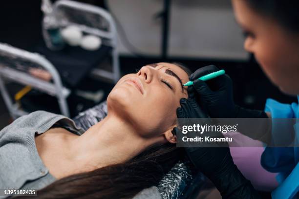 la femme millénaire est dans le studio de tatouage. sa pigmentation permanente des sourcils sera réalisée par un tatoueur professionnel - henné photos et images de collection