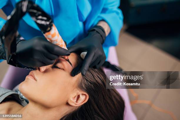 close-up on the face of a woman to whom a tattoo artist is doing permanent eyebrow pigmentation - beauty treatment stock pictures, royalty-free photos & images