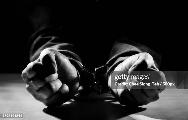 arrested criminal hands locked in handcuffs,close-up of man wearing sunglasses on table - prosecution stock pictures, royalty-free photos & images