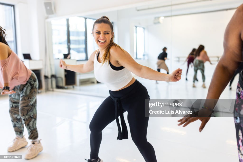 Smiling woman teaching zumba dance to students in fitness studio