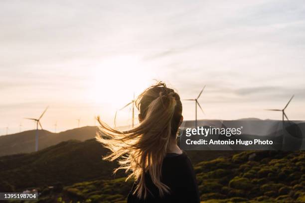 woman contemplating a windmill farm at sunset. - cleantech stock pictures, royalty-free photos & images