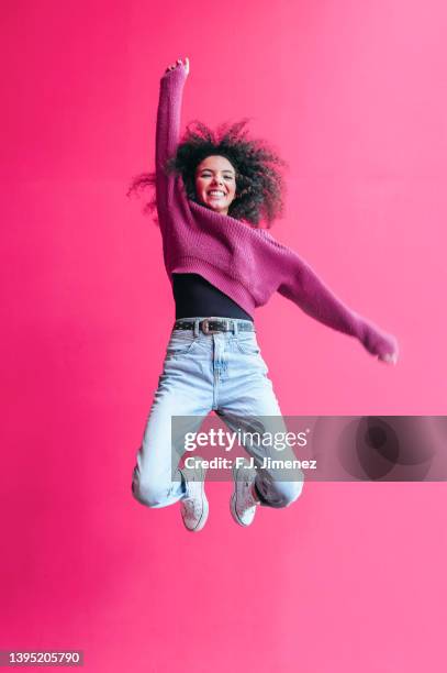 smiling woman jumping on pink background - personne qui saute de joie photos et images de collection