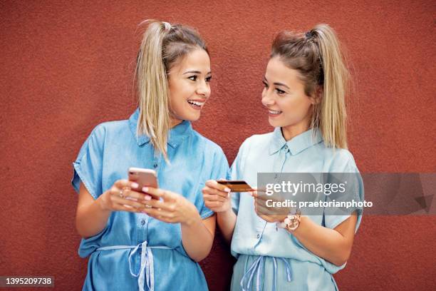 happy twin sisters are shopping online using smart phone and credit card - multiple birth stock pictures, royalty-free photos & images