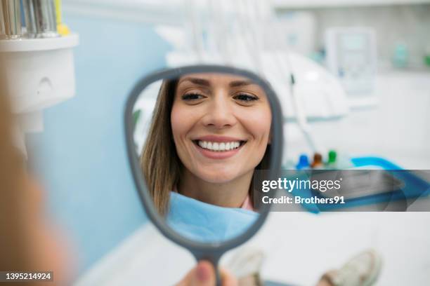 una donna felice che si guarda nello specchio tenuto in mano - denti foto e immagini stock