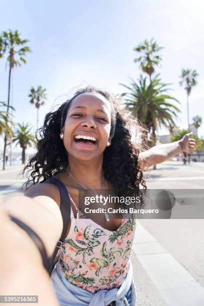 vertical photo of a traveler woman taking a selfie with a palm trees background. - selfi stock-fotos und bilder