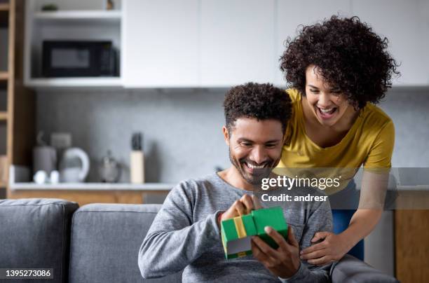 happy woman at home surprising man with a gift - opening door stockfoto's en -beelden