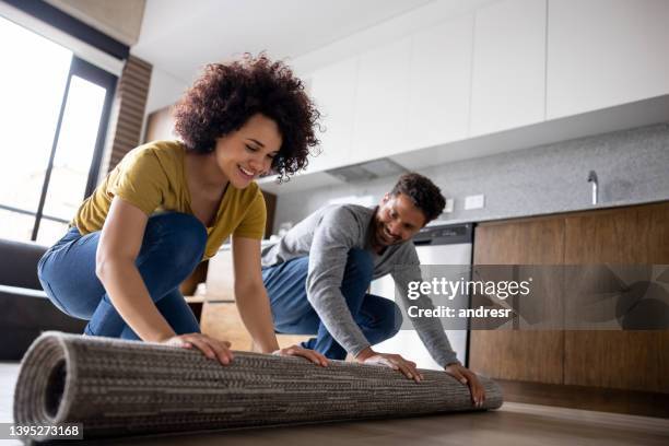 happy couple unrolling a carpet at home - home renovation stock pictures, royalty-free photos & images