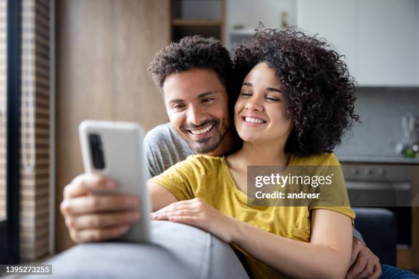 happy couple watching funny videos at home on a cell phone - happy couple using cellphone stockfoto's en -beelden