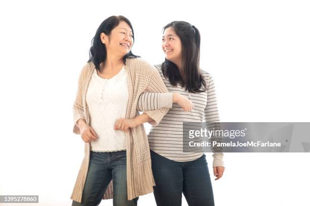 mature asian mother linking arms with eurasian daughter, white background - arm in arm stock pictures, royalty-free photos & images