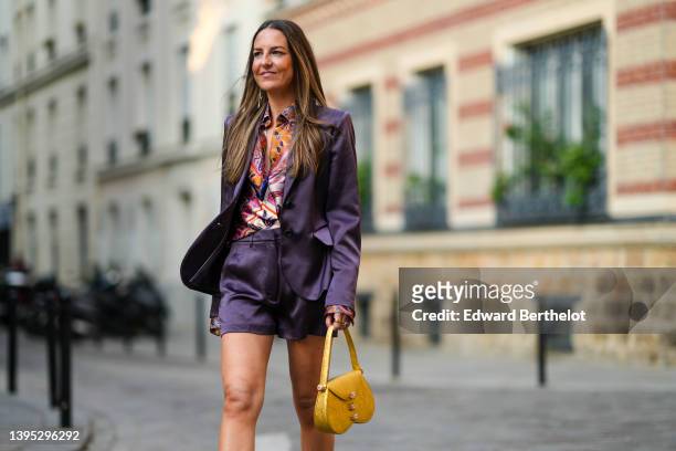 Alba Garavito Torre wears gold earrings, an orange with blue / black / pink print pattern silk shirt from Barbara Bui, a dark purple satin blazer...