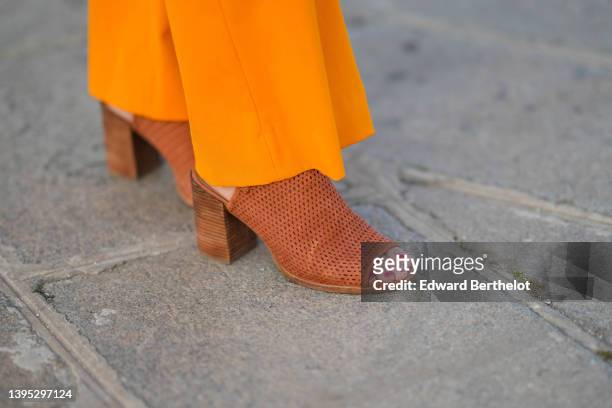 Amanda Derhy wears high waist orange flared suit pants, brown suede cut-out pattern block heels mules / shoes with open toe-cap, during a street...