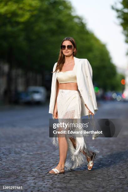 Diane Batoukina wears brown sunglasses from Dior, a white silk cropped top from Martin Martin, a white oversized linen blazer jacket from Zara, a...
