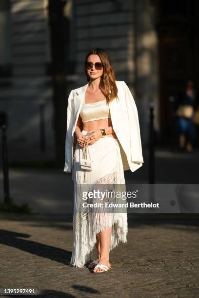 Diane Batoukina wears brown sunglasses from Dior, a white silk cropped top from Martin Martin, a white oversized linen blazer jacket from Zara, a...