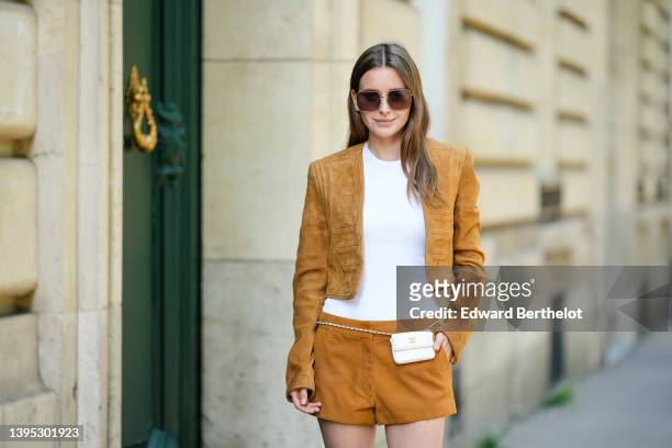 Diane Batoukina wears brown sunglasses from Dior, a white t-shirt from Anine Bing, a brown suede cropped jacket from Saint Laurent, matching suede...