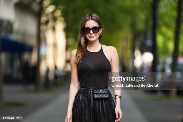 Diane Batoukina wears black sunglasses a black ribbed halter-neck tank-top, a high waist black pleated / accordion shiny leather long skirt from...