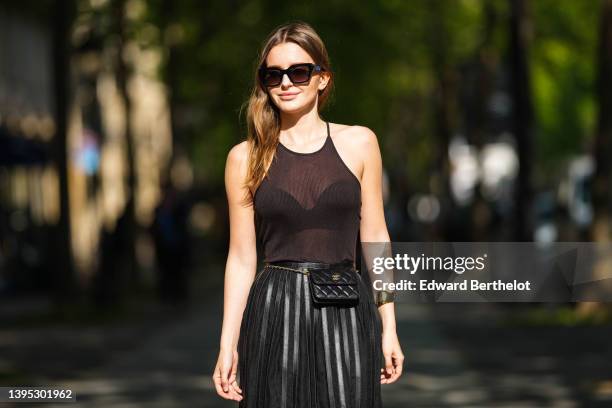 Diane Batoukina wears black sunglasses a black ribbed halter-neck tank-top, a high waist black pleated / accordion shiny leather long skirt from...