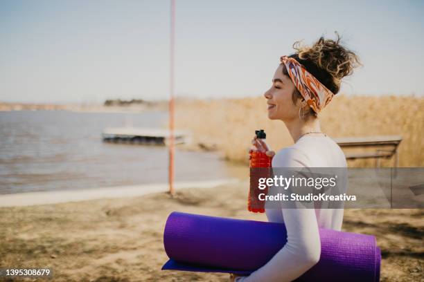 joven sonriente con una botella de jugo y una esterilla de yoga al aire libre - yogi fotografías e imágenes de stock