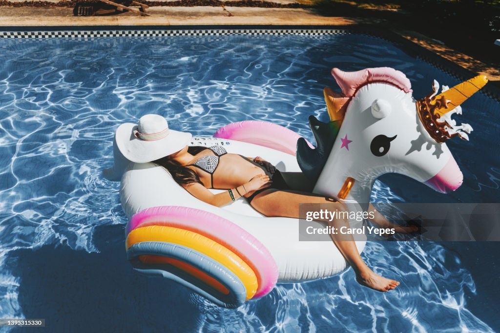 Young woman playing in a big unicorn inflatable ring at pool in summer