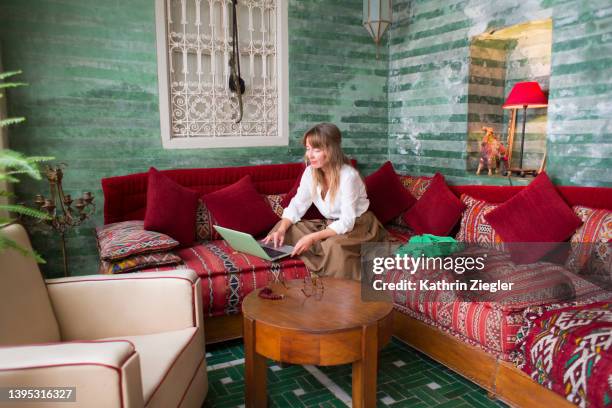 woman using laptop in lounge area of moroccan riad - maroc business stock-fotos und bilder