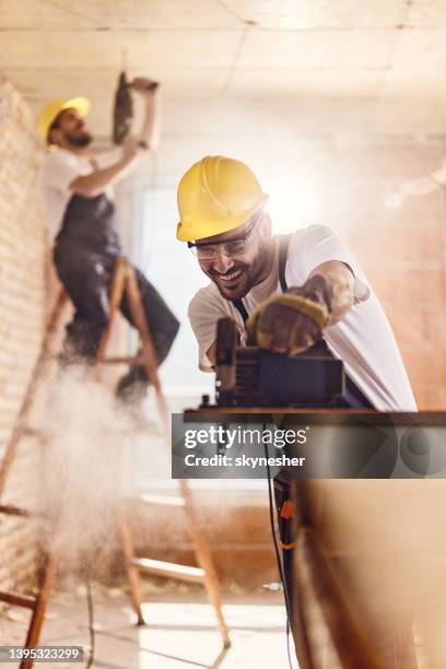 happy carpenter cutting wood plank with electric saw at construction site. - wood accuracy stock pictures, royalty-free photos & images