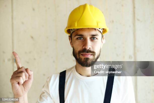junger bauarbeiter zeigt auf leere wand. - zeigefinger stock-fotos und bilder
