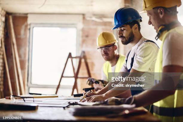 equipo de trabajadores manuales examinando el proyecto de vivienda mientras trabajan en la obra. - construcción fotografías e imágenes de stock