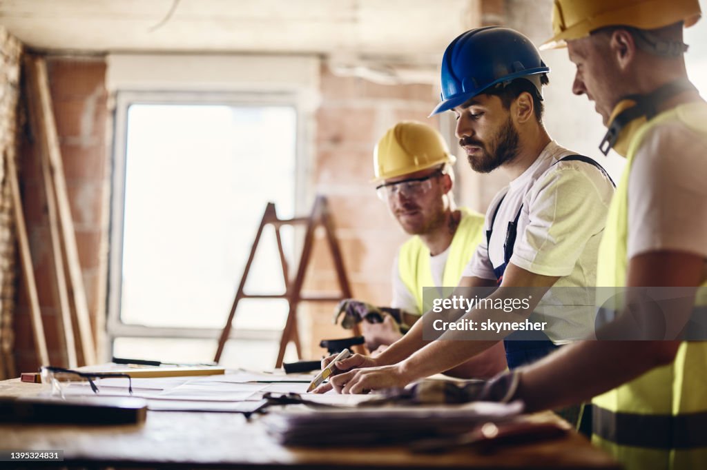 Team di operai che esaminano il progetto abitativo mentre lavorano in cantiere.