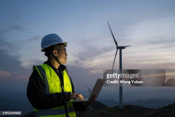 an asian male electrical maintenance worker is standing at a wind power plant with a laptop in the evening - confidence male landscape stock-fotos und bilder