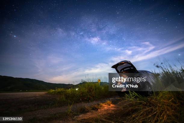 young beauty female sit behind suv car vehicle and relax with book in weekend under beautiful milky way with star in night sky - astronomie stock-fotos und bilder