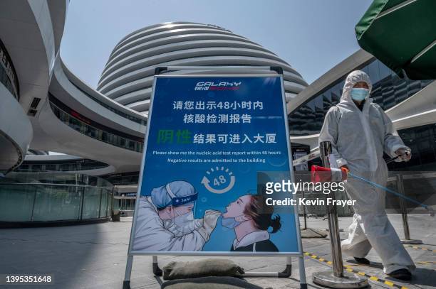 Worker sprays as he disinfects the area around a nucleic acid testing site to detect COVID-19 as a sign reminds customers they must show a negative...