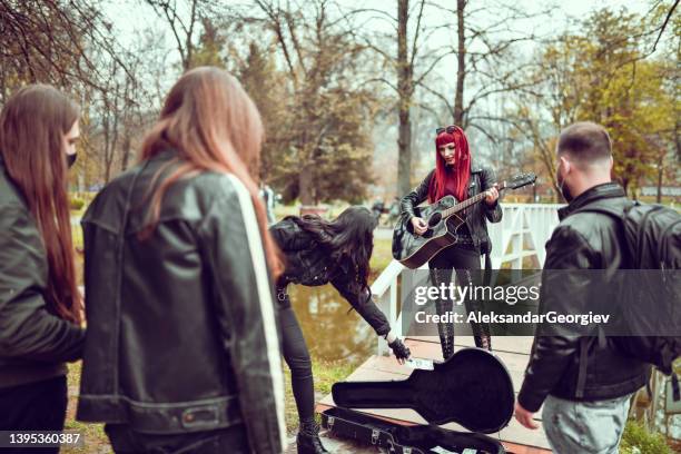 gothic redhead female earning cash during busking performance in park - masked musicians bildbanksfoton och bilder