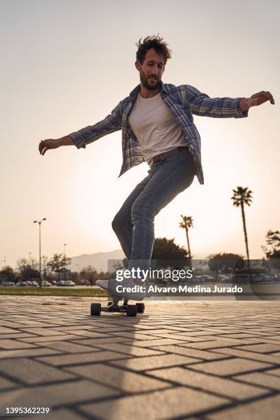 young man dressed in casual clothes skateboarding with a longboard skateboard in the city at sunset. concept of lifestyle and skating - men's free skate imagens e fotografias de stock