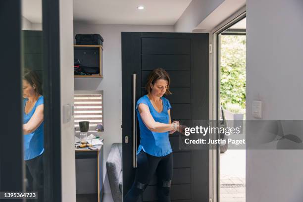 mature woman checks her smartwatch by her front door before she heads off for a run - une seule femme d'âge mûr photos et images de collection