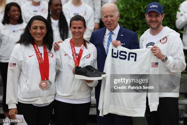 President Joe Biden is given a pair of shoes and a Team USA shirt by Olympic bobsledder Elana Meyers Taylor, Olympic Speedskater Brittany Bowe and...