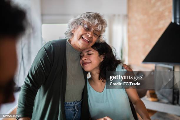 grandmother embracing granddaughter at home - hispanic grandmother stock pictures, royalty-free photos & images