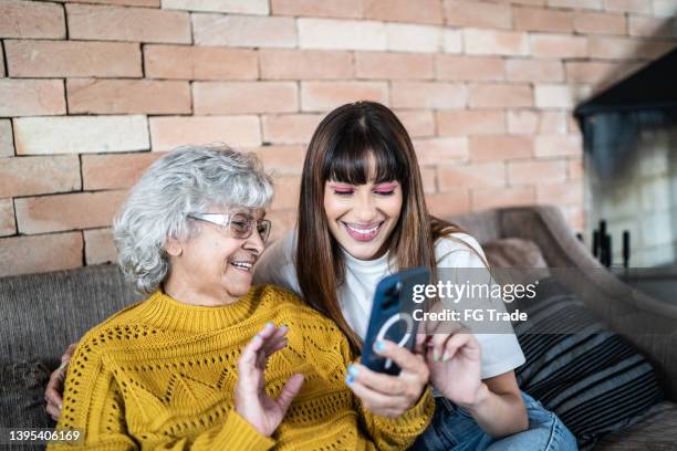 granddaughter and grandmother using mobile phone at home - young woman with grandmother stock pictures, royalty-free photos & images