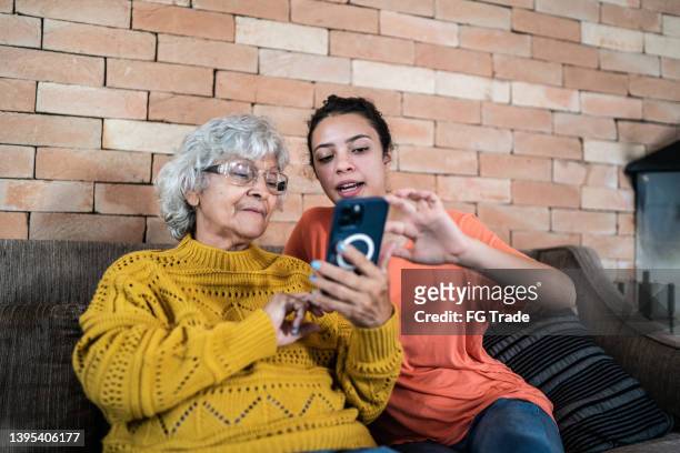 granddaughter helping grandmother to use the mobile phone at home - een helpende hand stockfoto's en -beelden