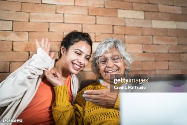 granddaughter and grandmother on a video call using laptop at home - lange afstandsrelatie stockfoto's en -beelden