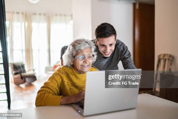 petit-fils et grand-mère utilisant un ordinateur portable à la maison - two generation family photos et images de collection